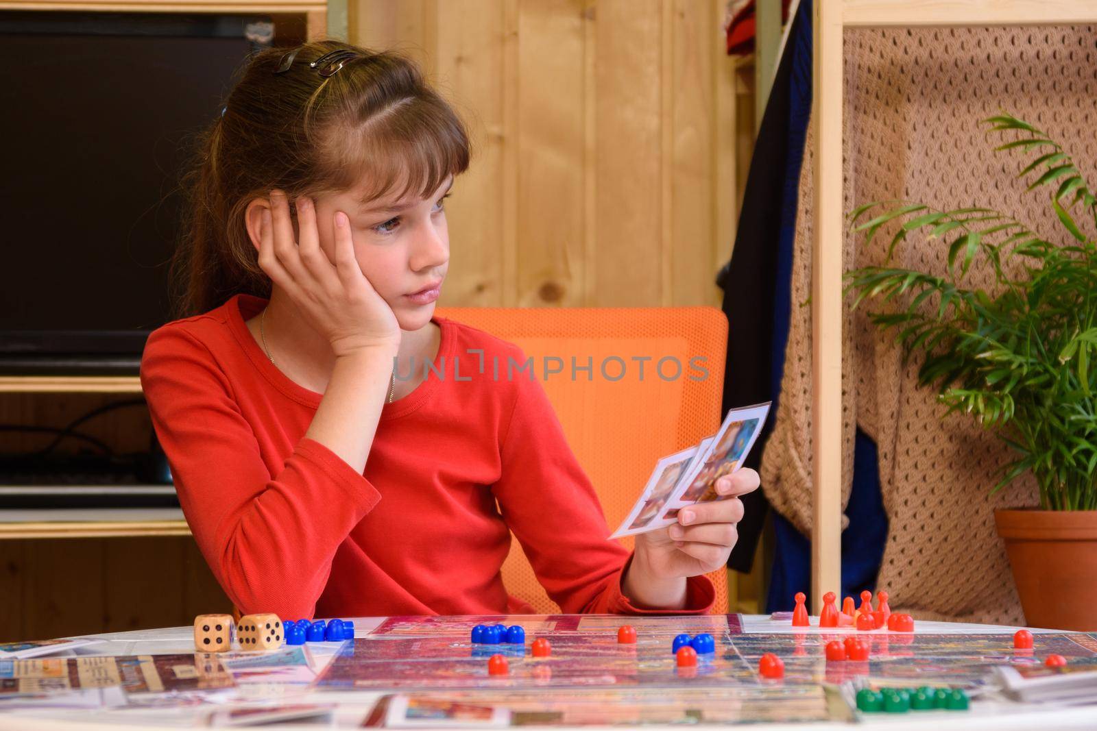 The girl plays board games and is thoughtful holding cards in her hand
