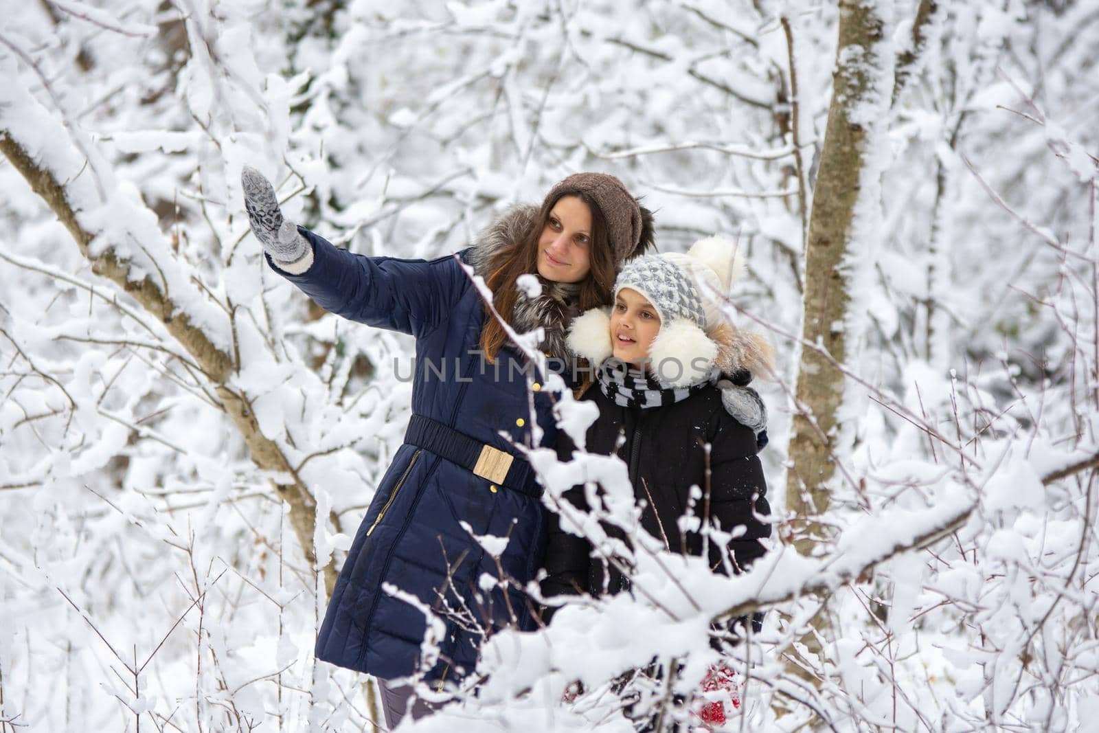 A girl and her daughter are walking through the snowy forest, the girl shows something interesting
