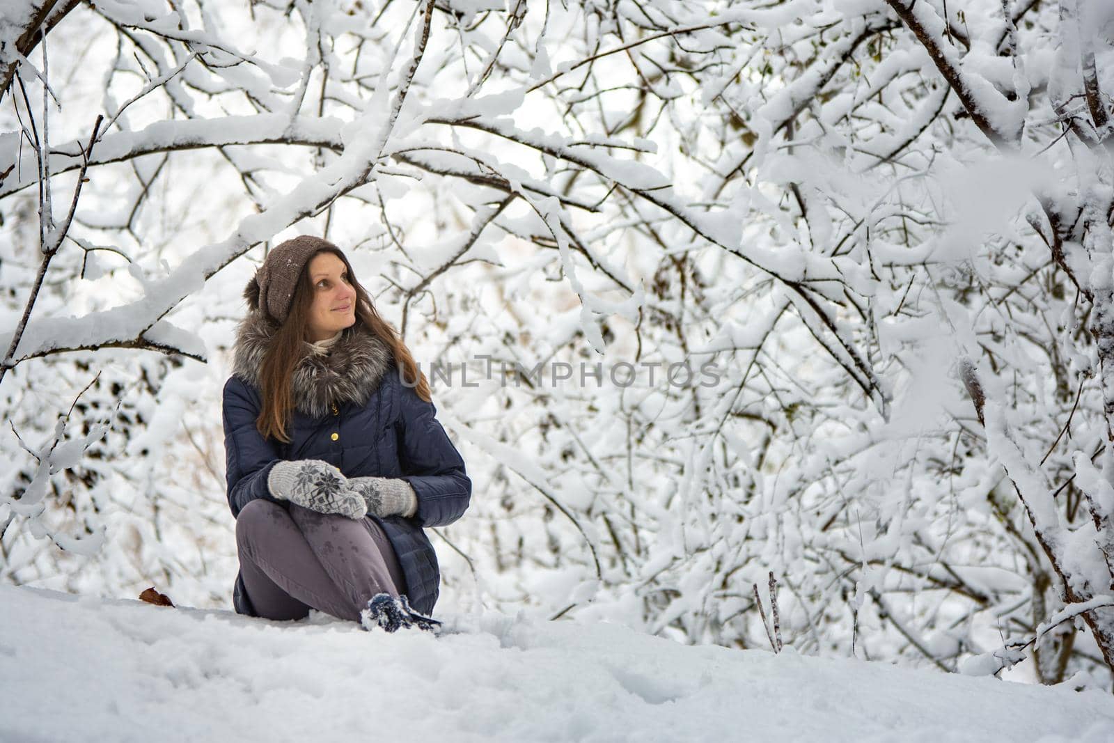 The girl sat down in a beautiful snowy forest and admires the beauty