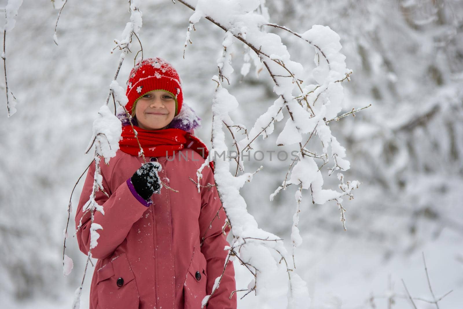 Happy girl stands in a snowy forest under a snowy branch by Madhourse
