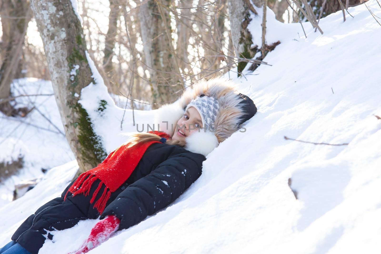 The girl fell into a snowdrift with her back and looked into the frame in a snowy forest