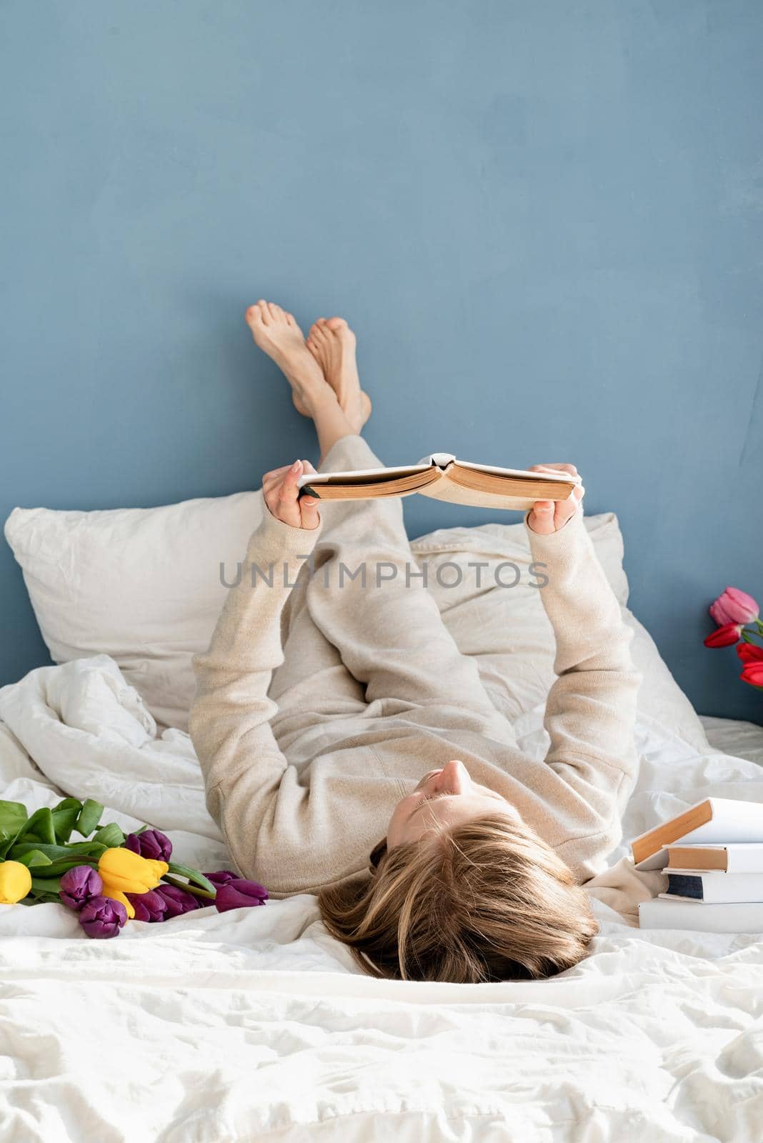 Happy woman sitting on the bed wearing pajamas reading a book by Desperada