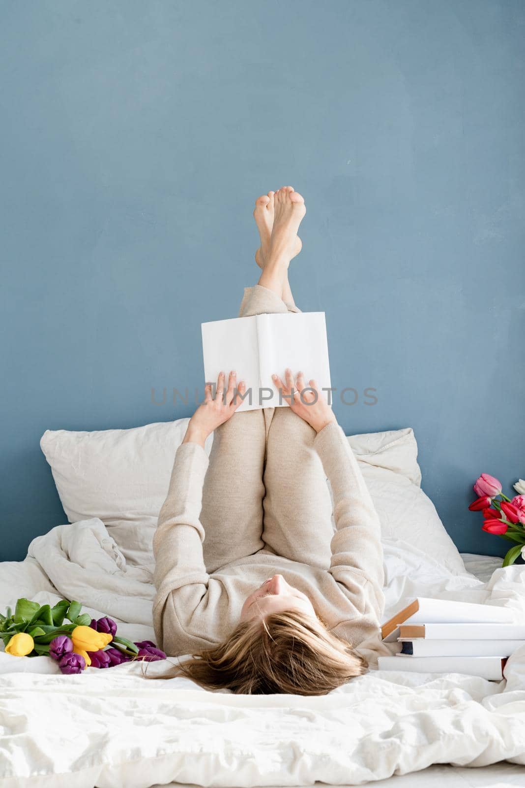 Happy woman lying on the bed wearing pajamas reading a book by Desperada