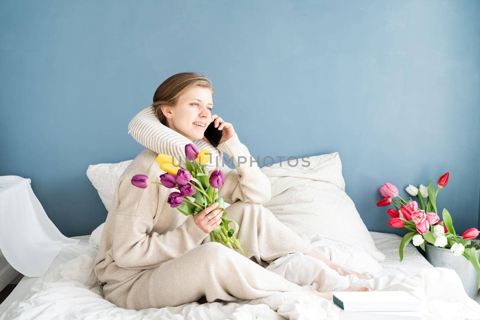 Happy woman sitting on the bed wearing pajamas talking on the phone by Desperada