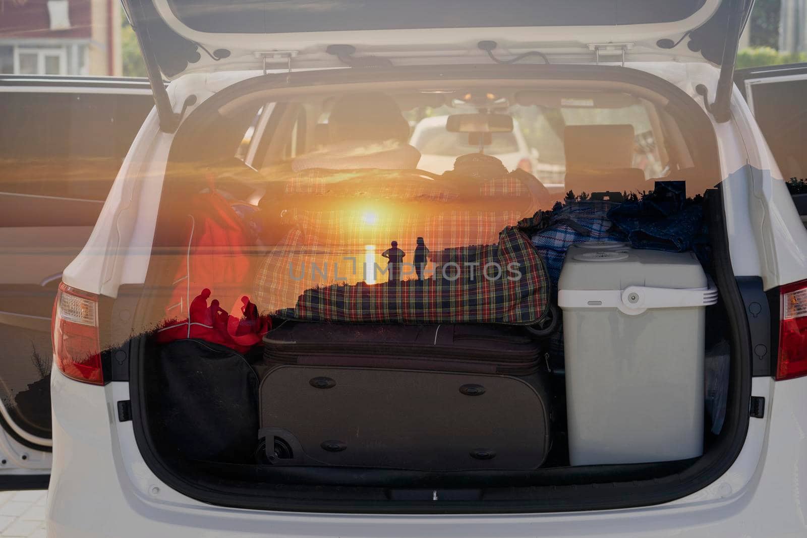 Double exposure of the car with things for traveling and sunset with silhouettes of people.