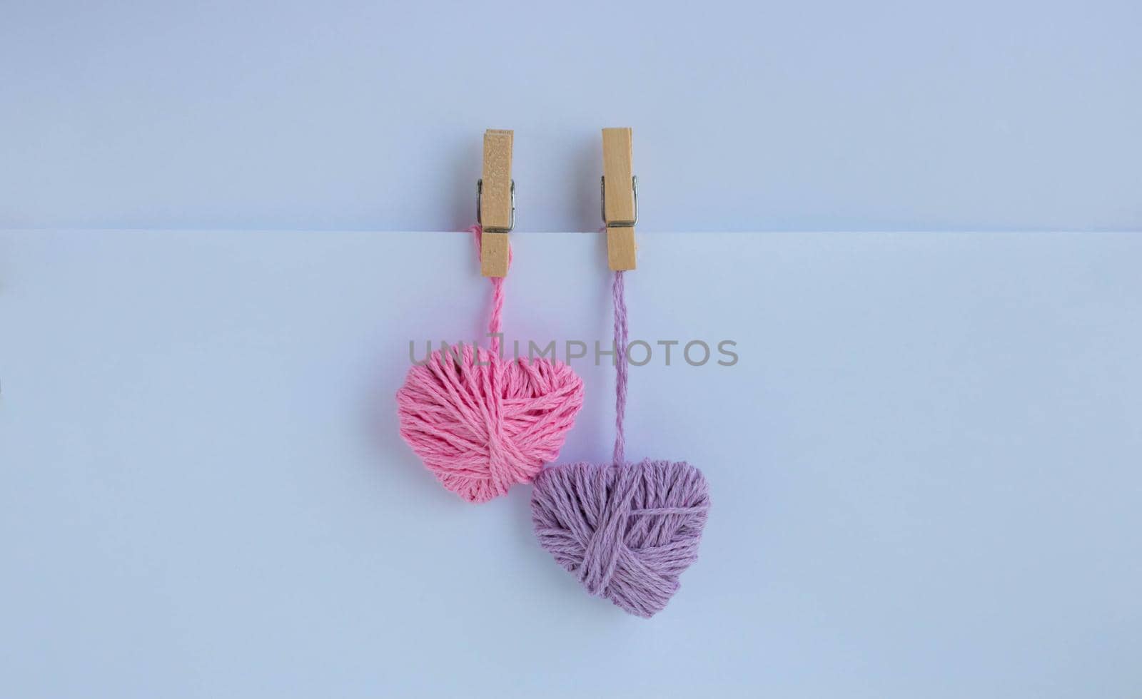 Two hearts of thread hang with clothespins on a paper pocket. Holiday card, background. The concept of Valentine's Day, March 8, Mother's Day.