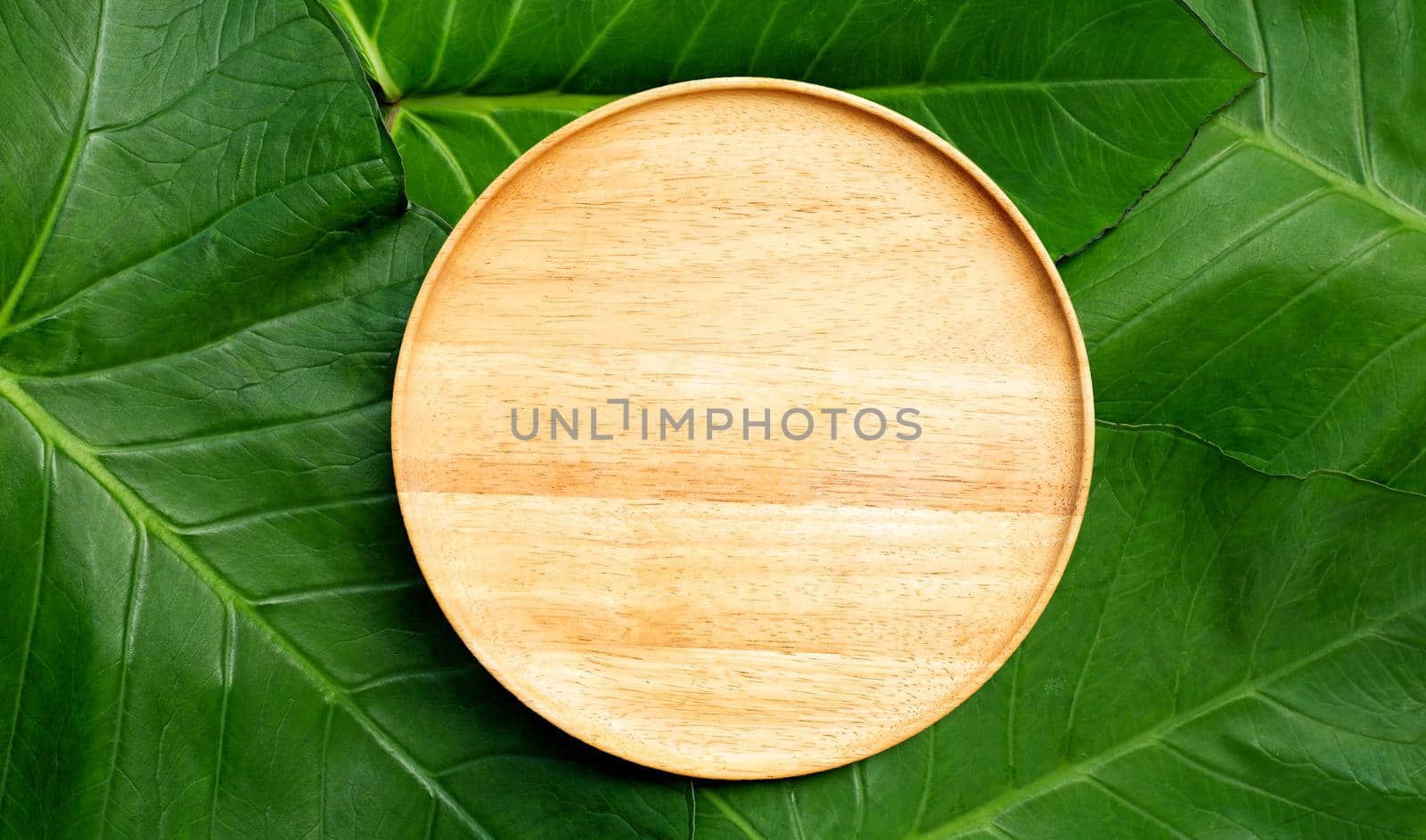 Empty wooden plate on taro leaves background. Top view