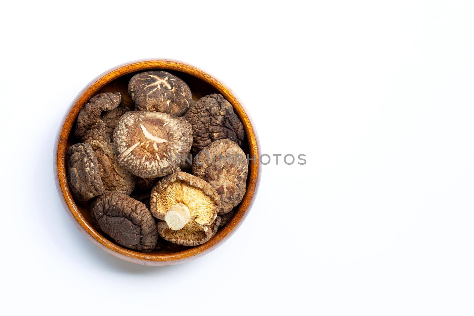 Dried shiitake mushrooms in wooden bowl on white background.
