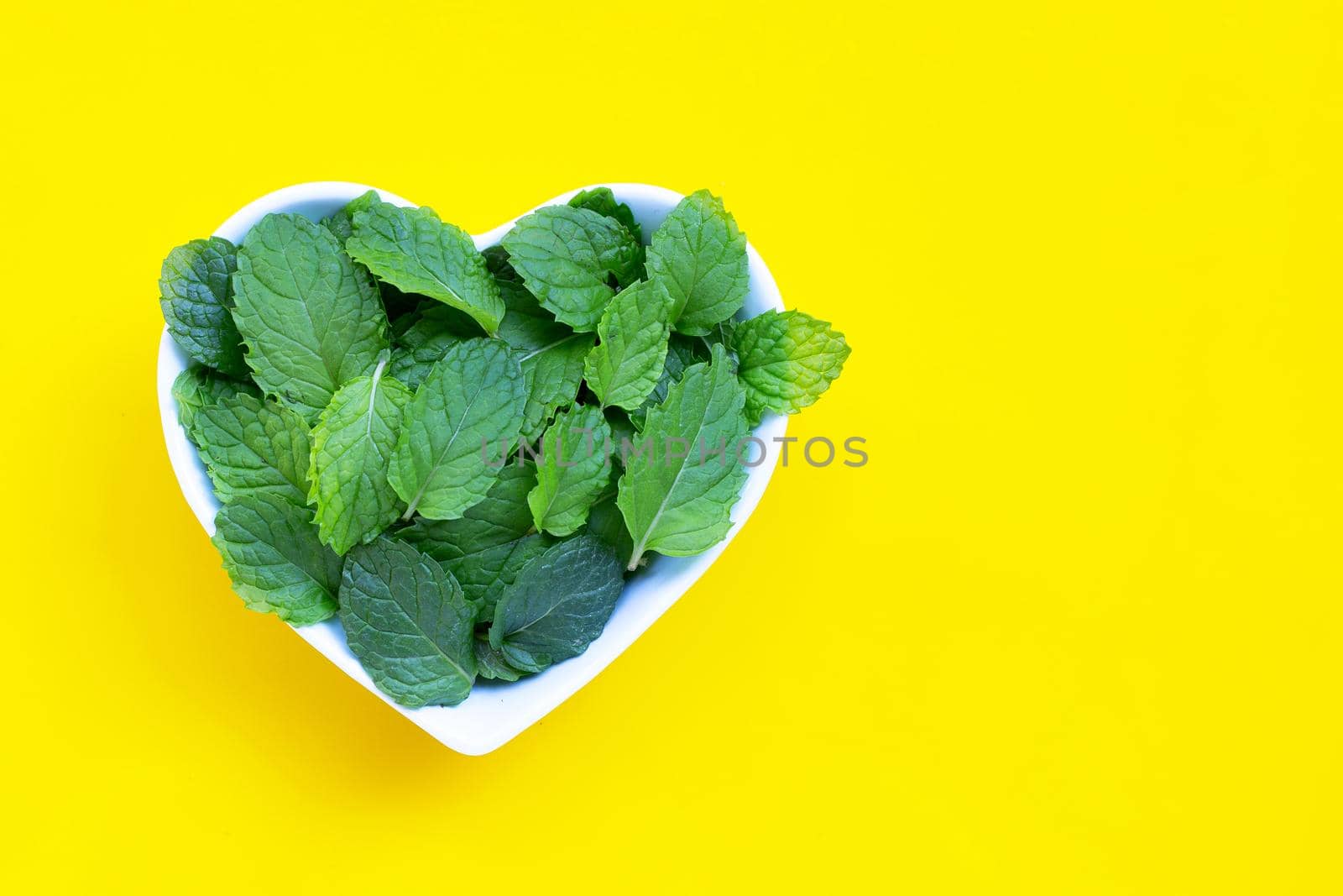 Fresh mint leaves in heart shape bowl on yelow background. Top view