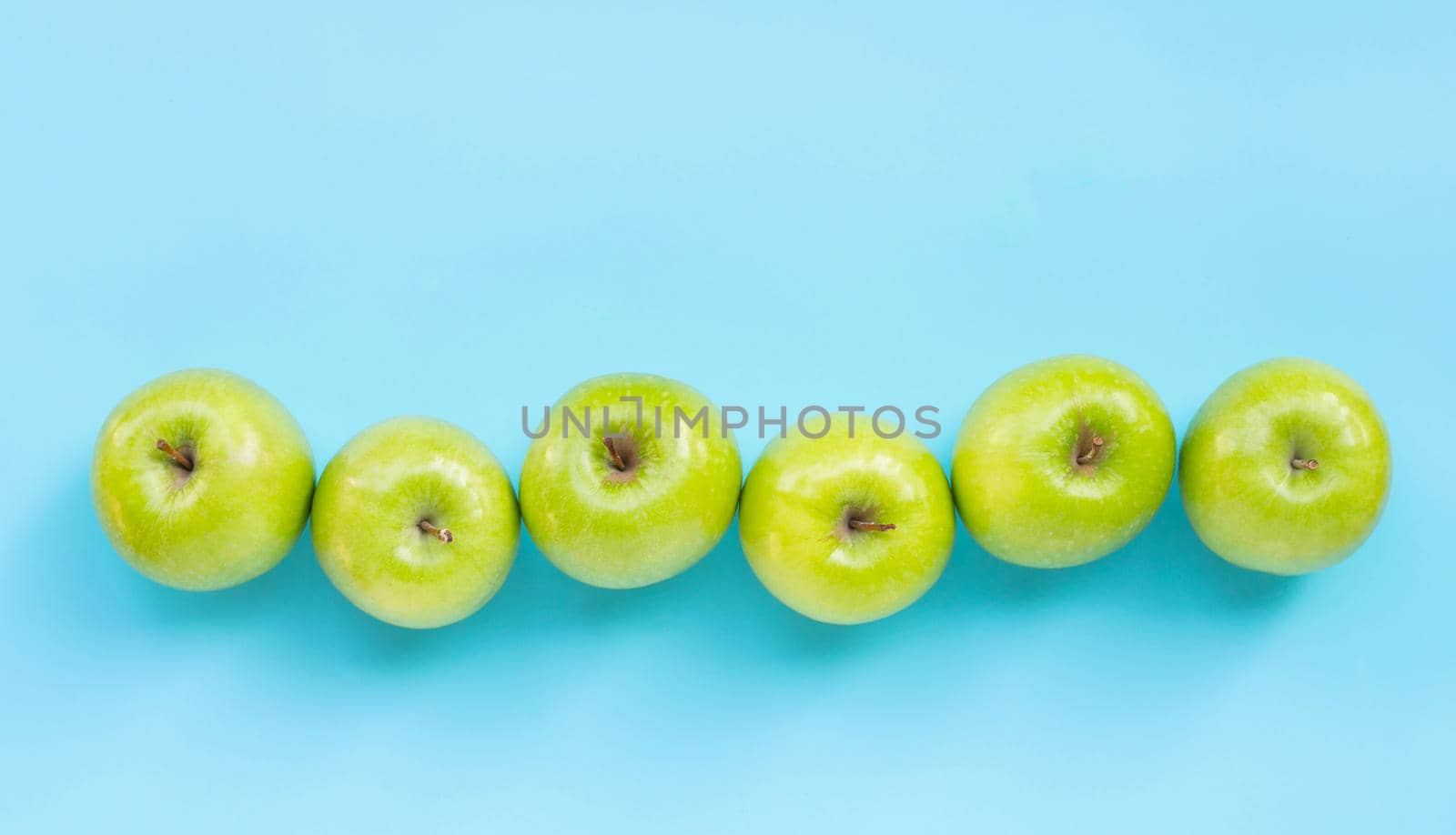 Green apples on blue background. Copy space