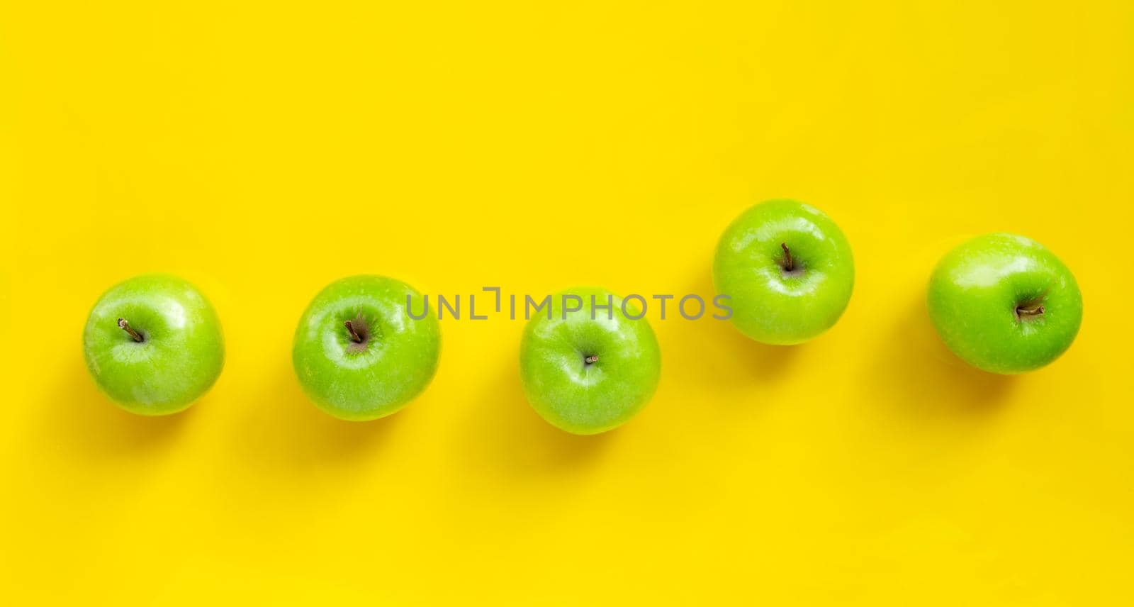 Green apples on yellow background. Copy space