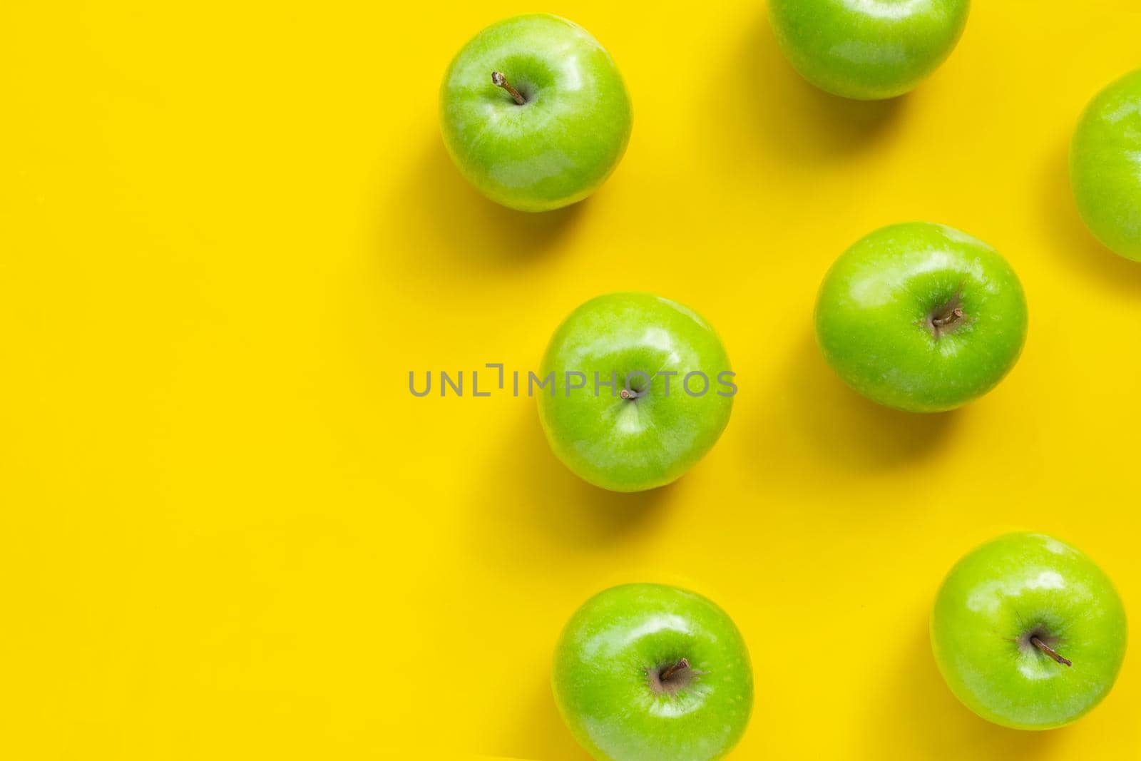 Green apples on yellow background. Copy space