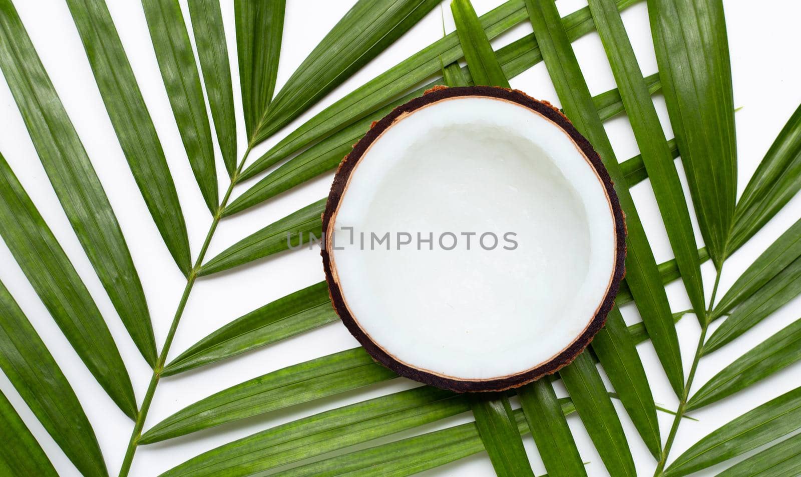 Half coconut on tropical palm leaves on white background. Top view