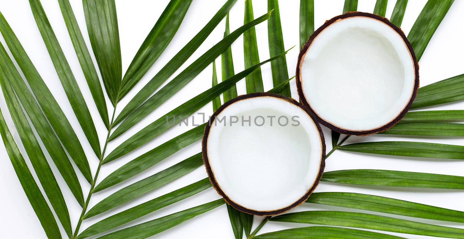 Half coconuts on tropical palm leaves on white background. Top view