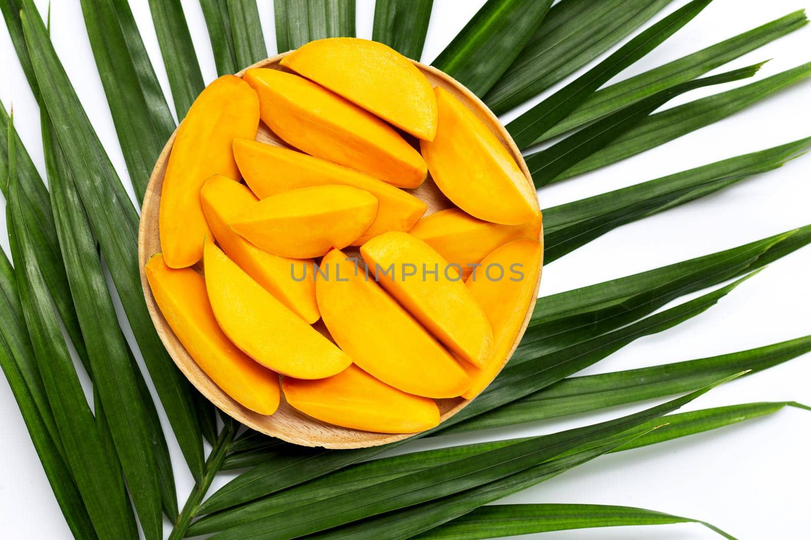 Mango slices on wooden plate on tropical palm leaves.