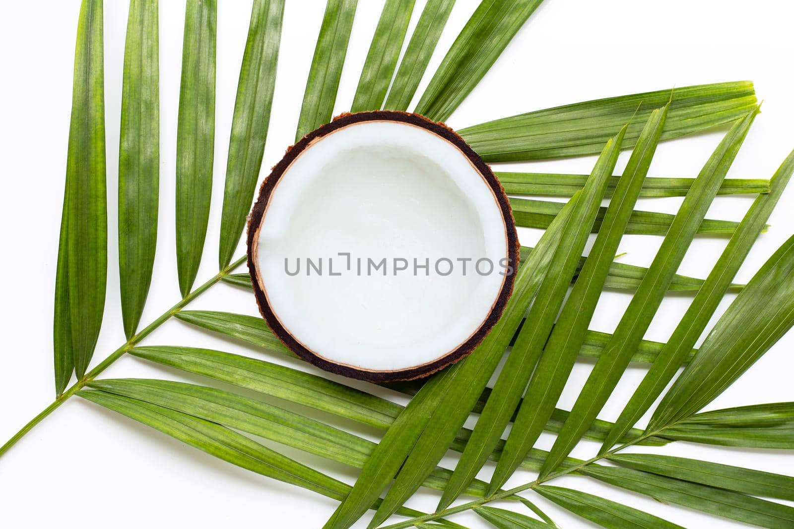 Half coconut on tropical palm leaves on white background. Top view
