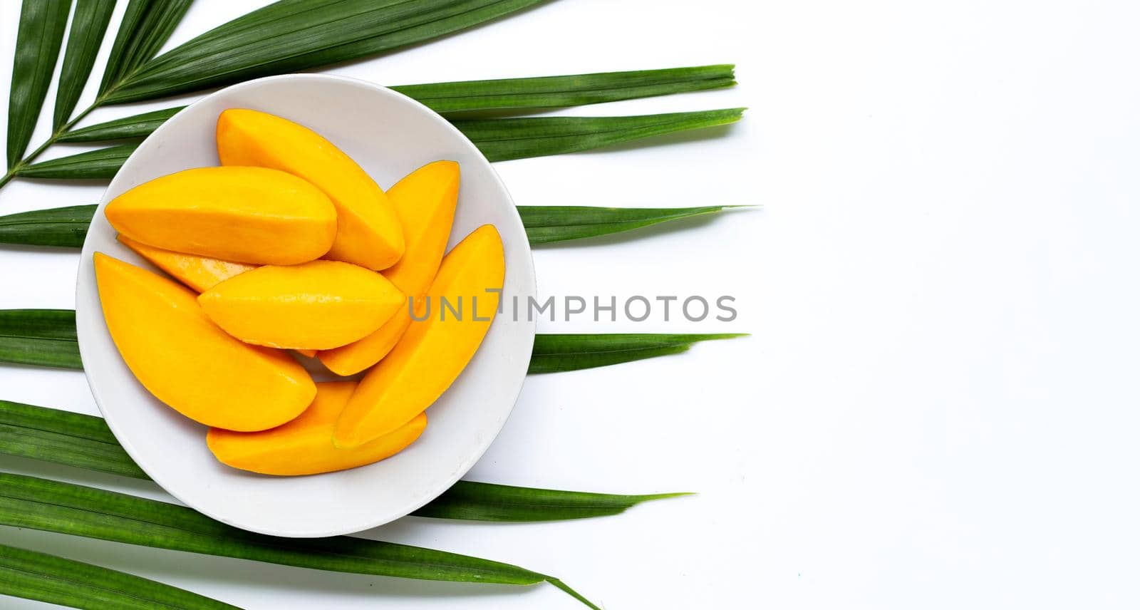 Mango slices on white plate on tropical palm leaves. Top view