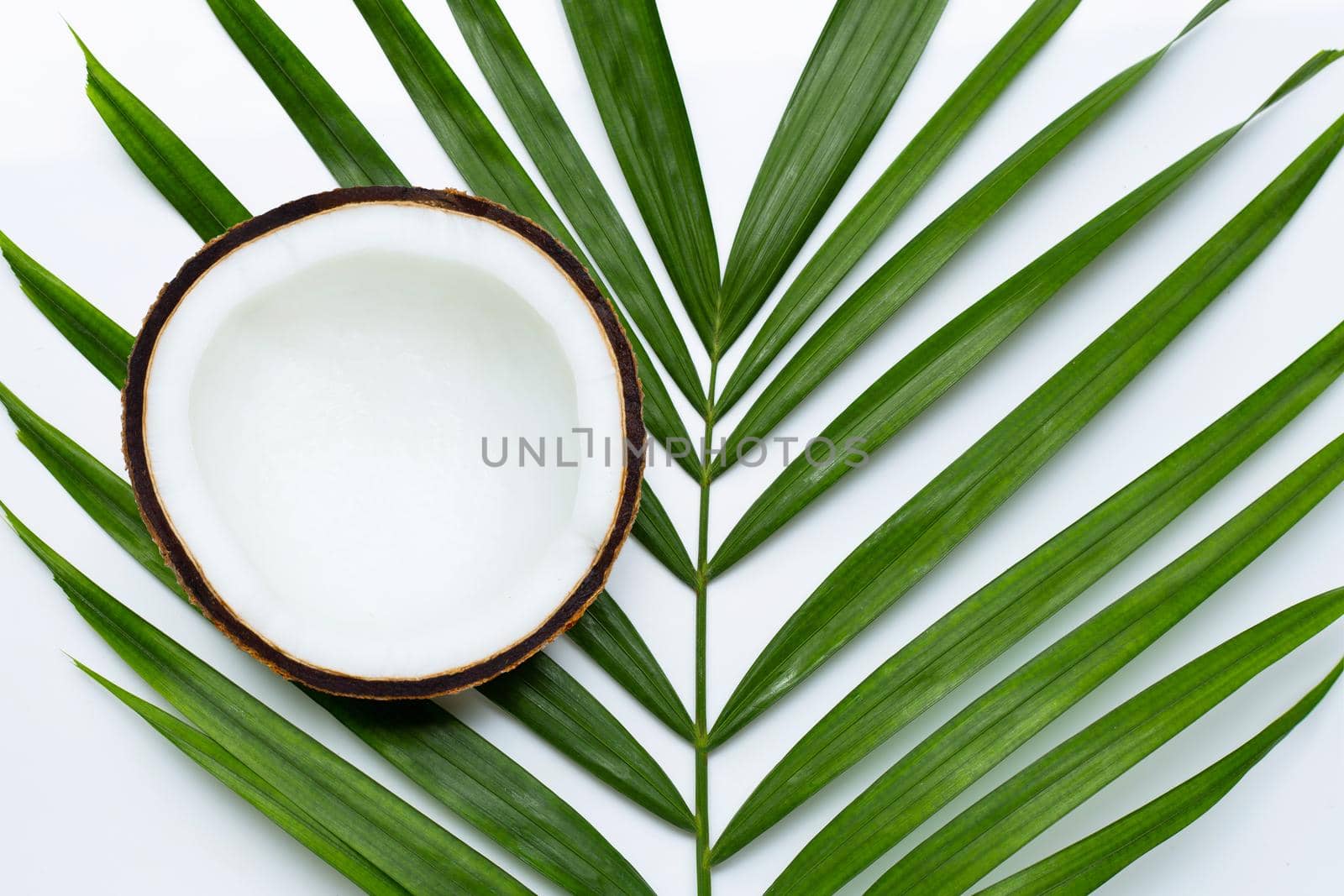 Half coconut on tropical palm leaves on white background. Top view