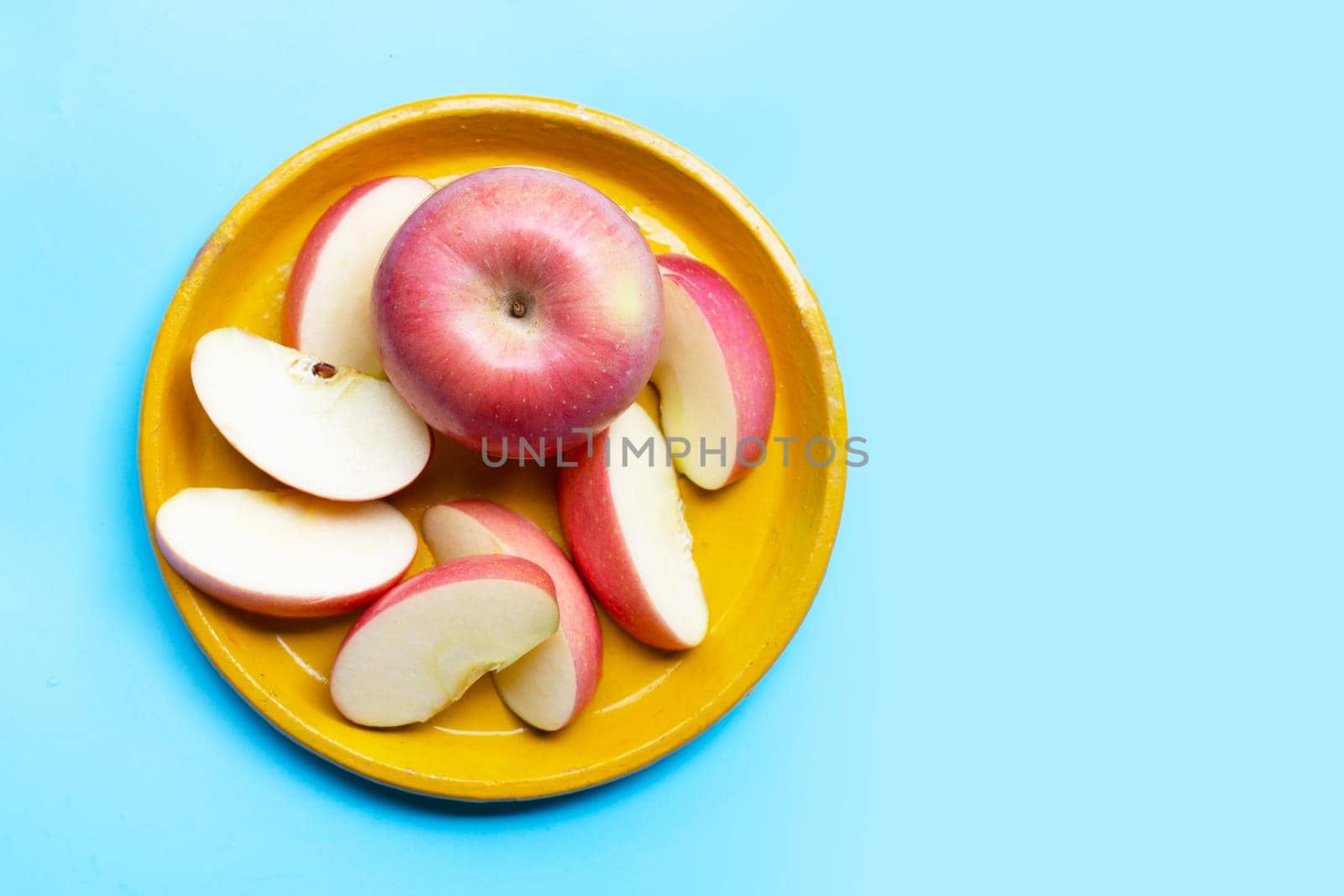 Fresh and juicy apples on yellow plat on blue background. Copy space
