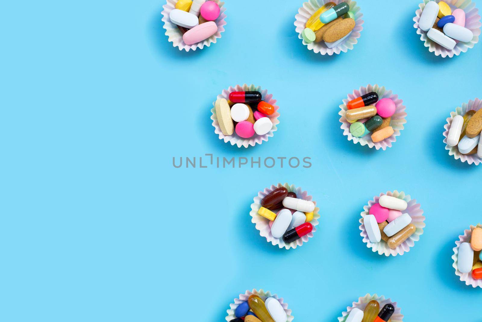 Colorful tablets with capsules and pills in cupcake wrappers on blue background.