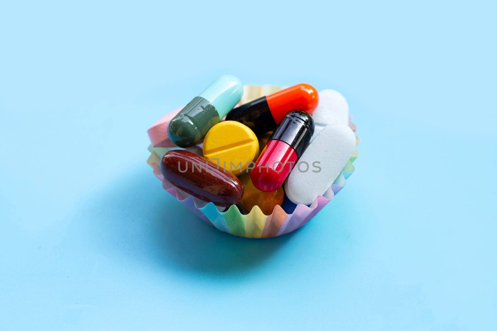 Colorful tablets with capsules and pills in cupcake wrappers on blue background.
