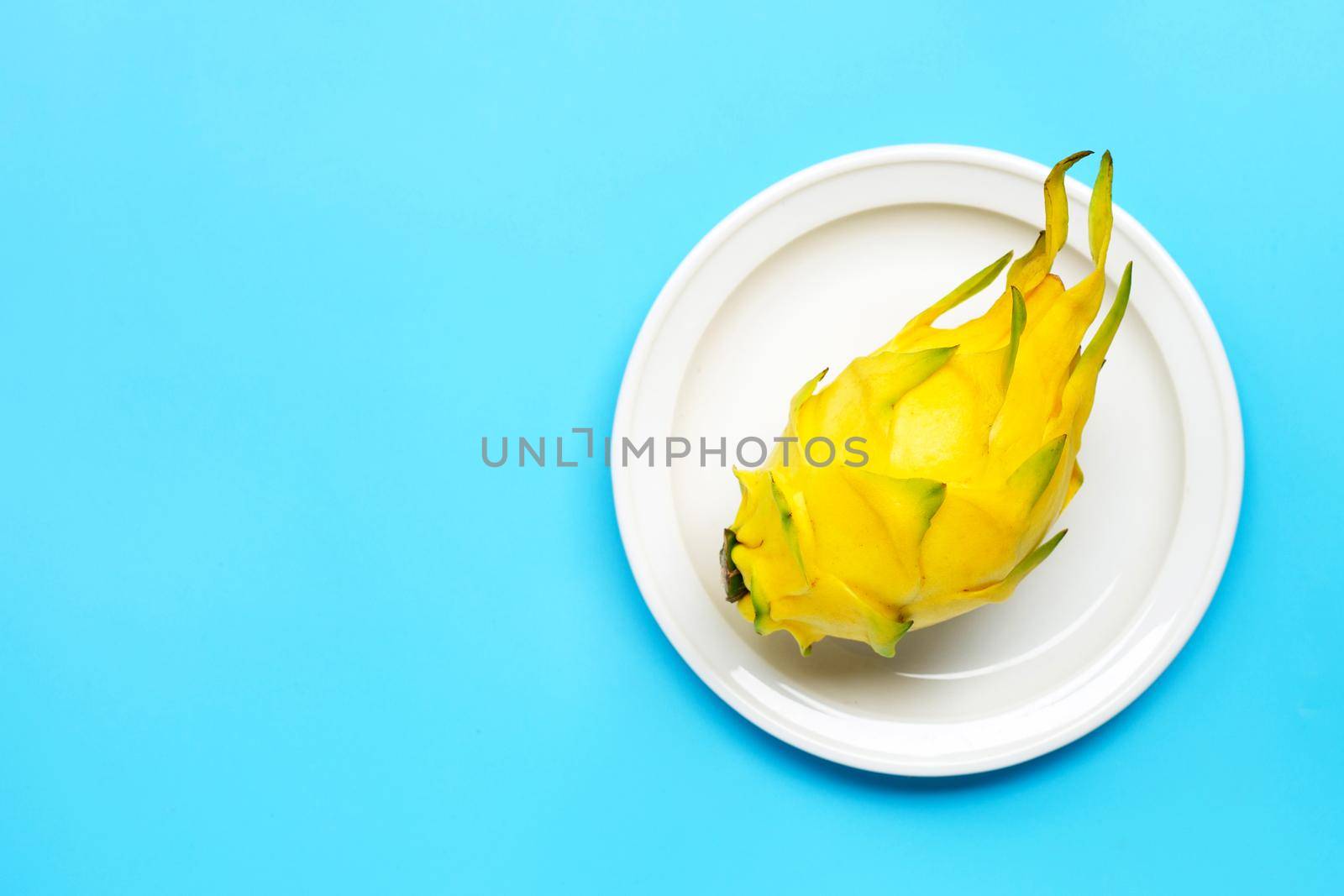 Yellow pitahaya or dragon fruit on white plate on blue background. Copy space