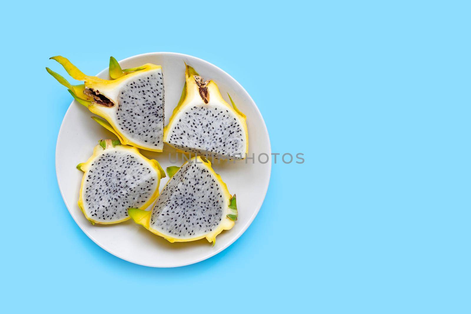 Yellow pitahaya or dragon fruit on white plate on blue background. Copy space