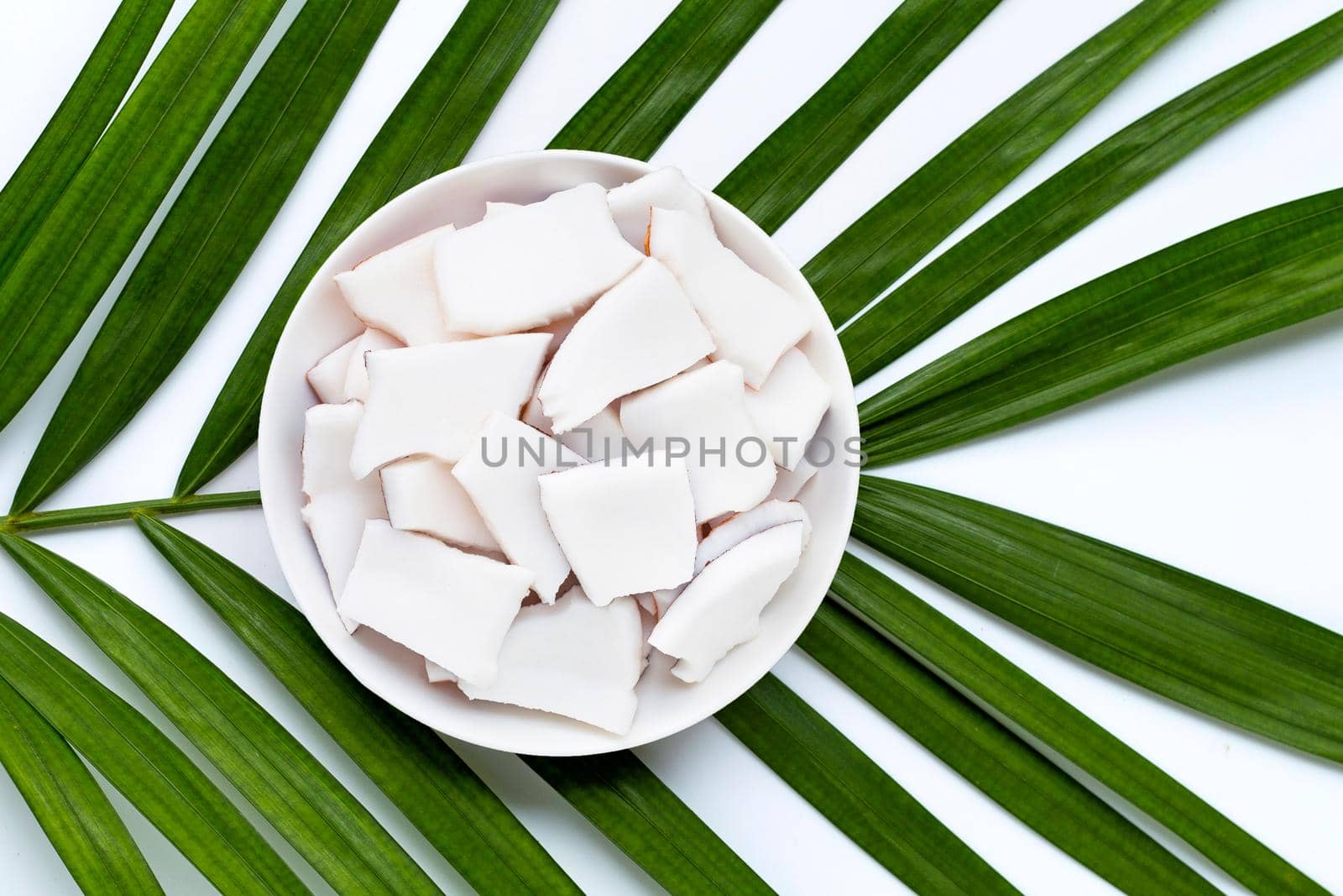 Coconut pieces on dish plate on tropical palm leaves. Top view