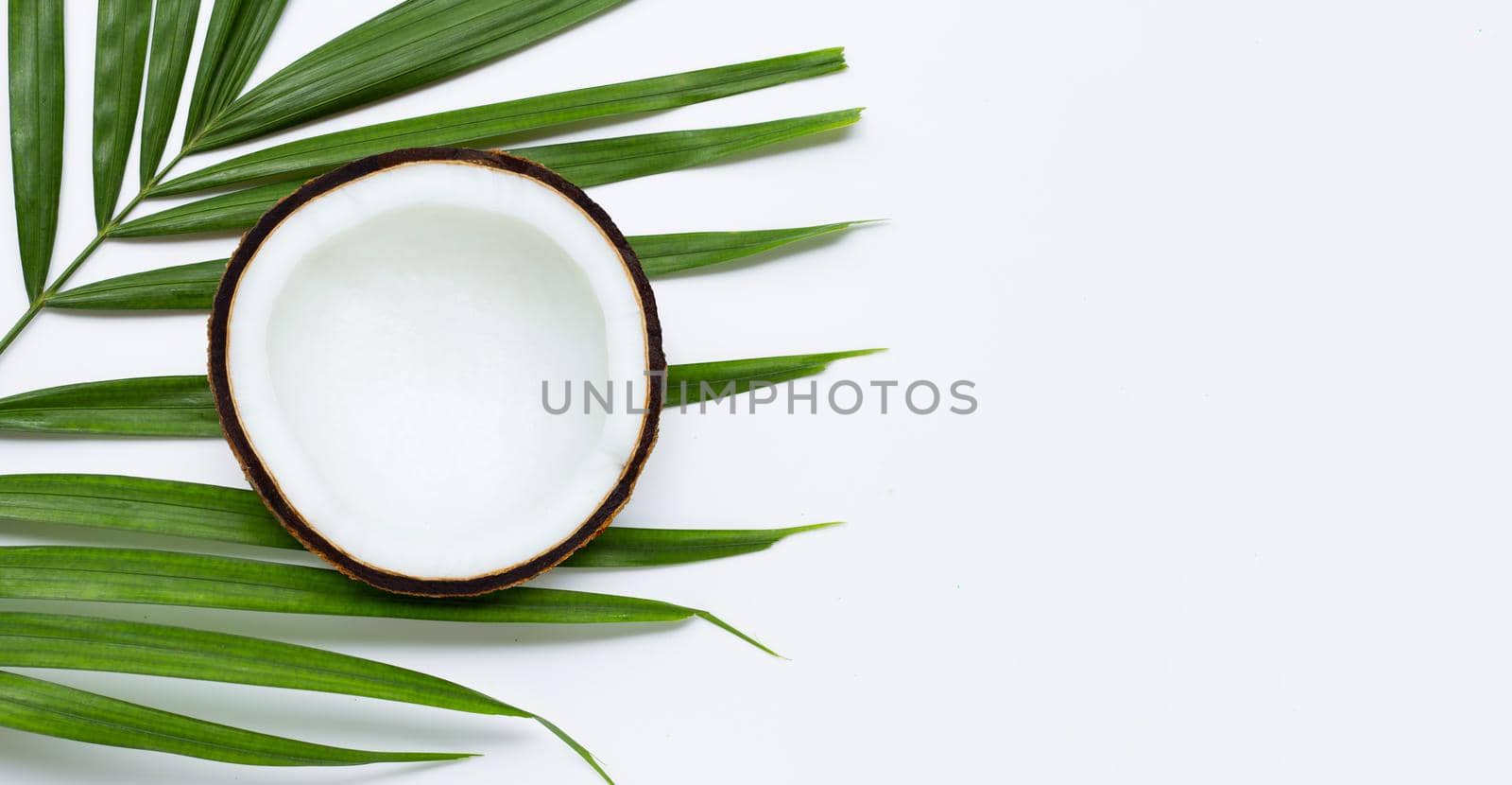 Half coconut on tropical palm leaves on white background. Top view