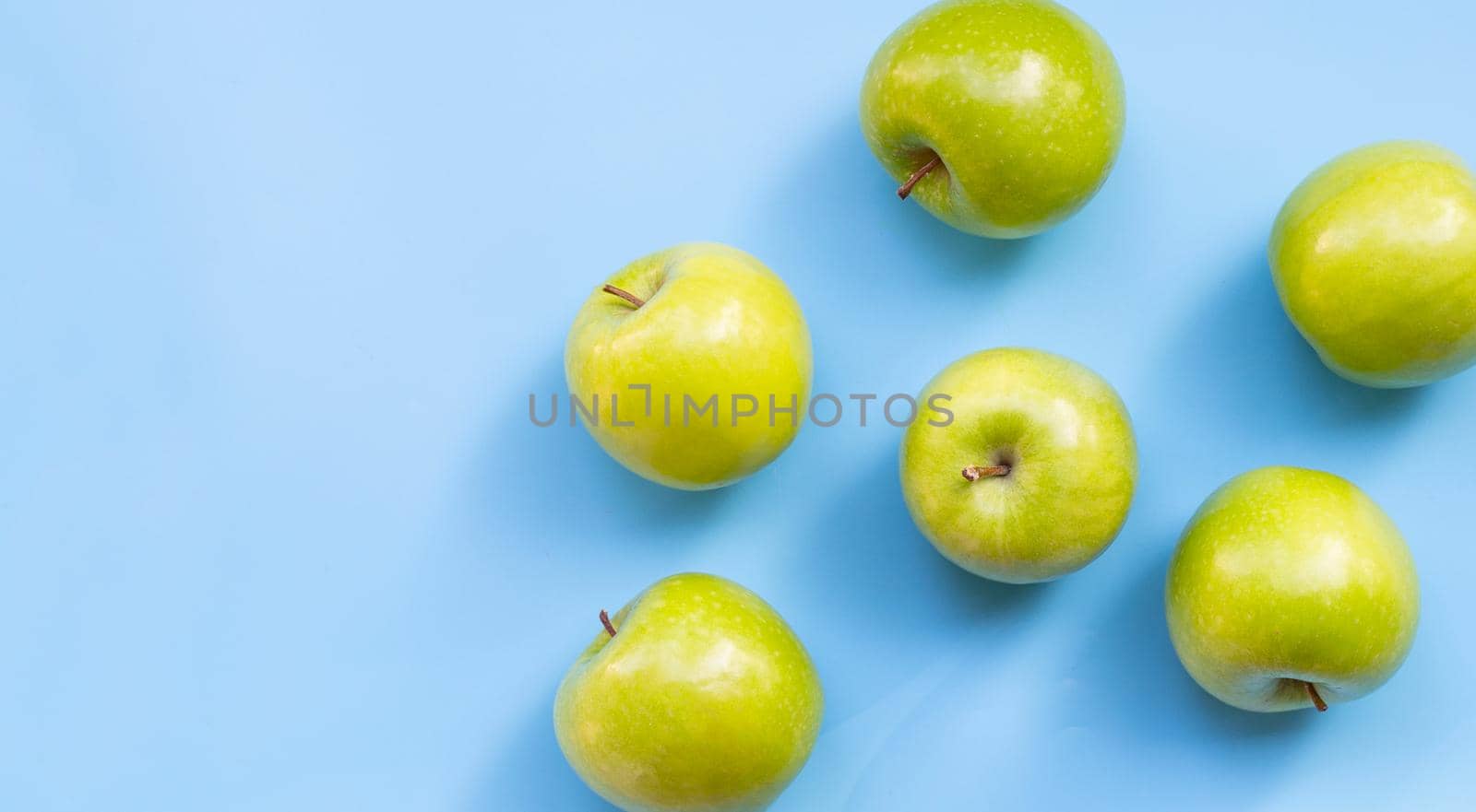 Green apples on blue background. Copy space