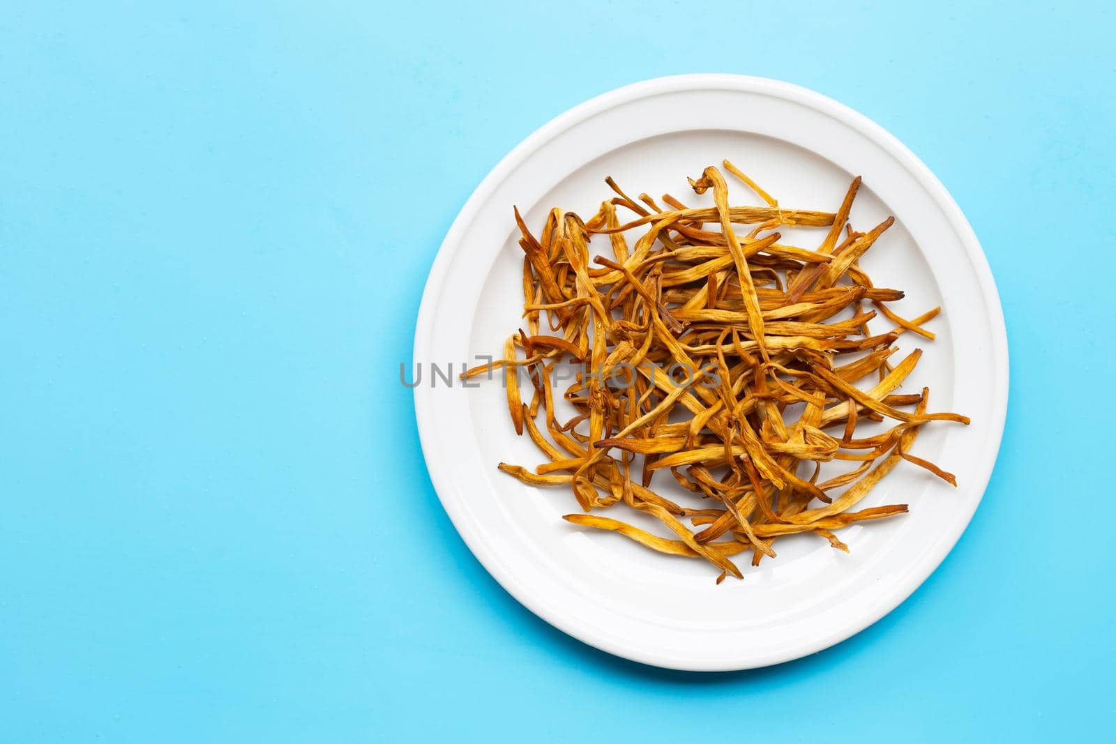 Dried Lily Buds on white plate on blue background. Copy space