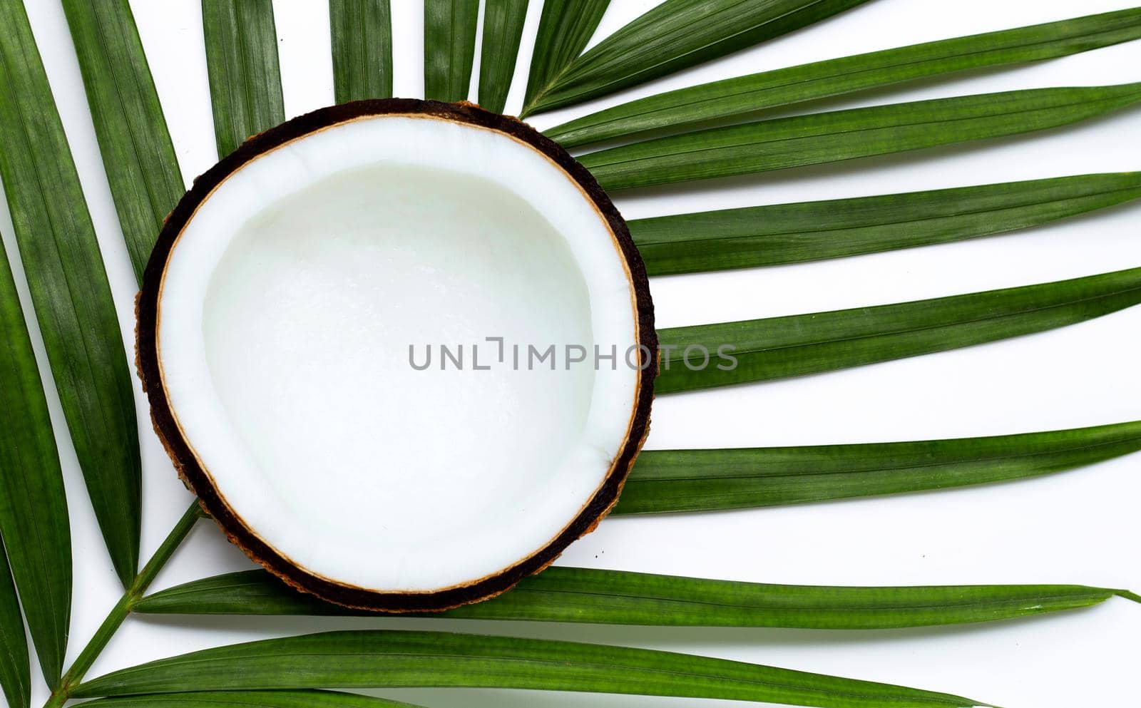 Half coconut on tropical palm leaves on white background. Top view