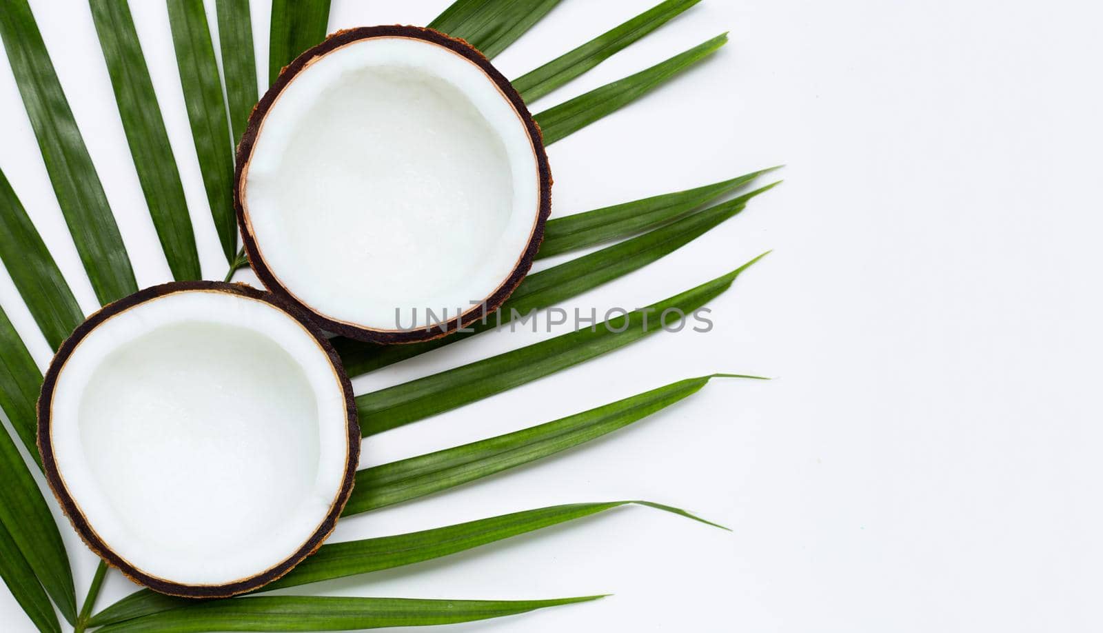 Half coconuts on tropical palm leaves on white background. Top view