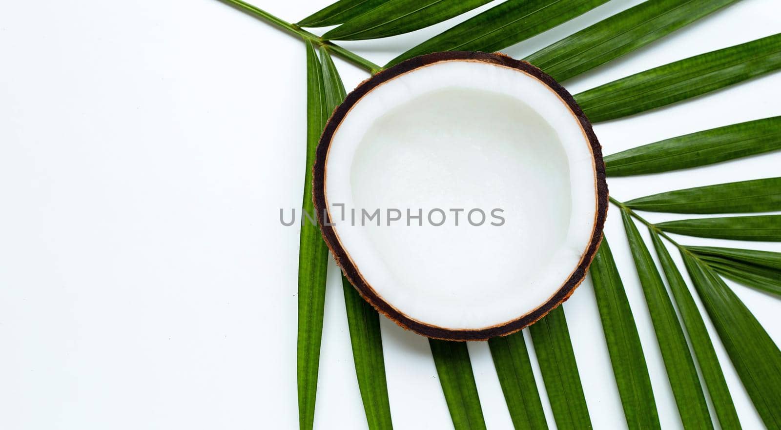 Half coconut on tropical palm leaves on white background. Top view