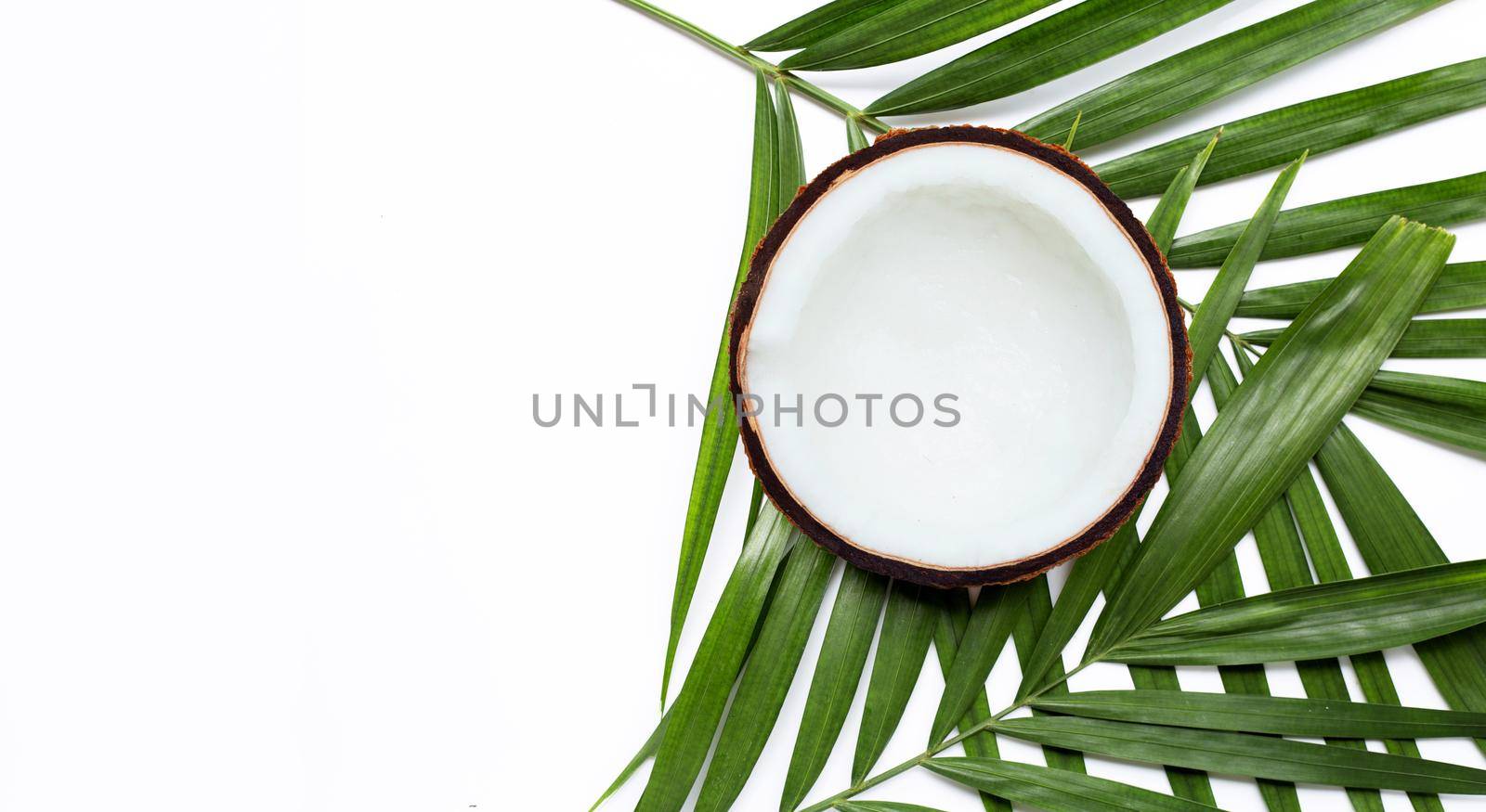 Half coconut on tropical palm leaves on white background. Top view