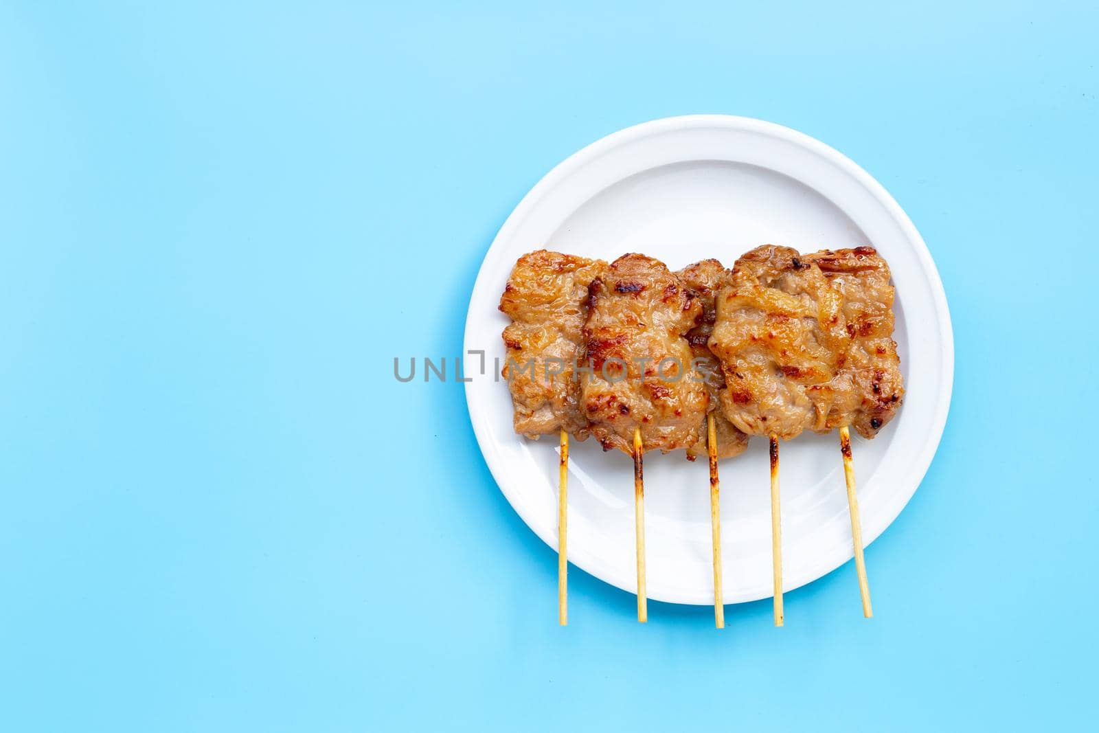 Grilled pork on white plate on blue background. Copy space