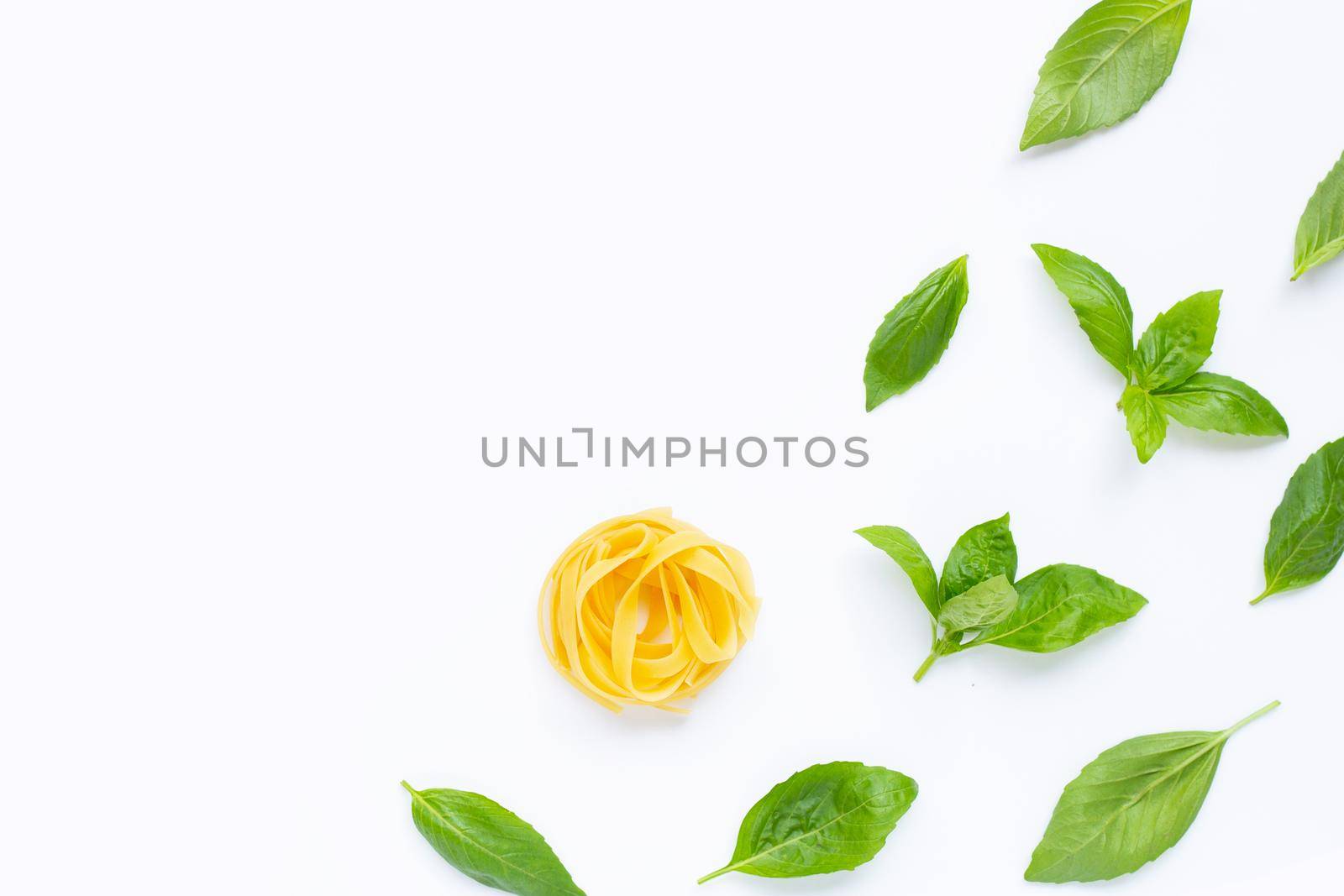 Raw tagliatelle pasta with basil leaves on white background.
