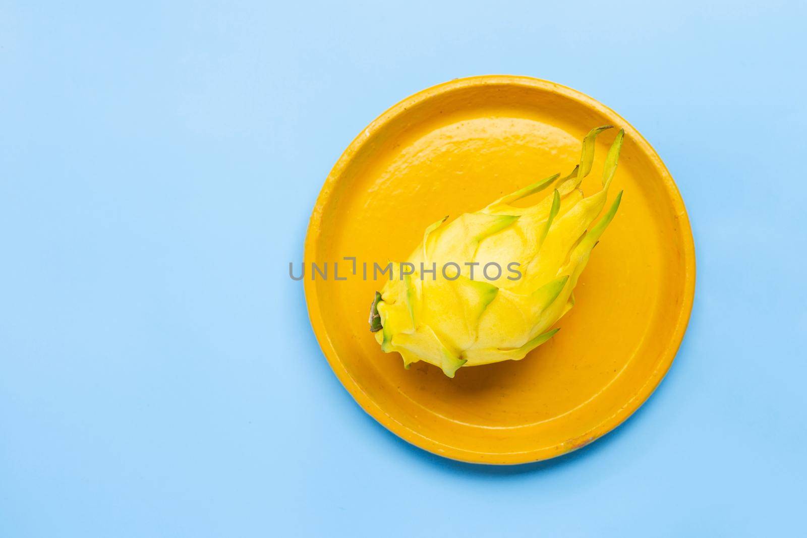 Yellow pitahaya or dragon fruit on yellow plate on blue background. Copy space