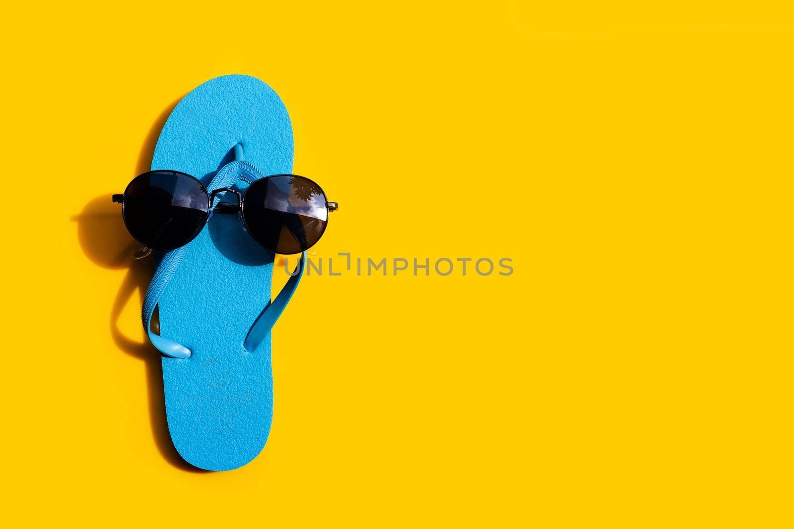 Blue flip flops with sunglasses on yellow background. Enjoy summer holiday concept.