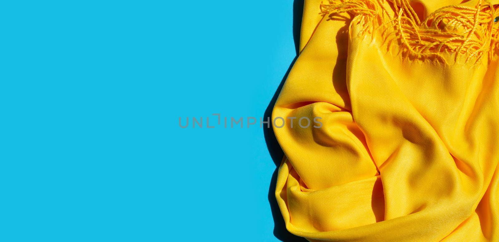 Yellow women's shawl on blue background. Copy space