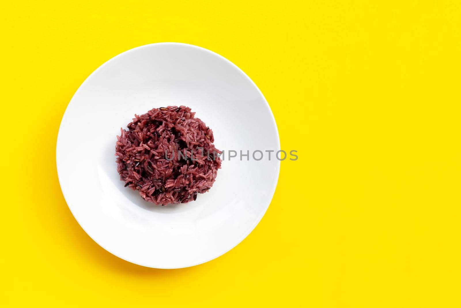Black sticky rice on white ceramic dish on yellow background. Copy space