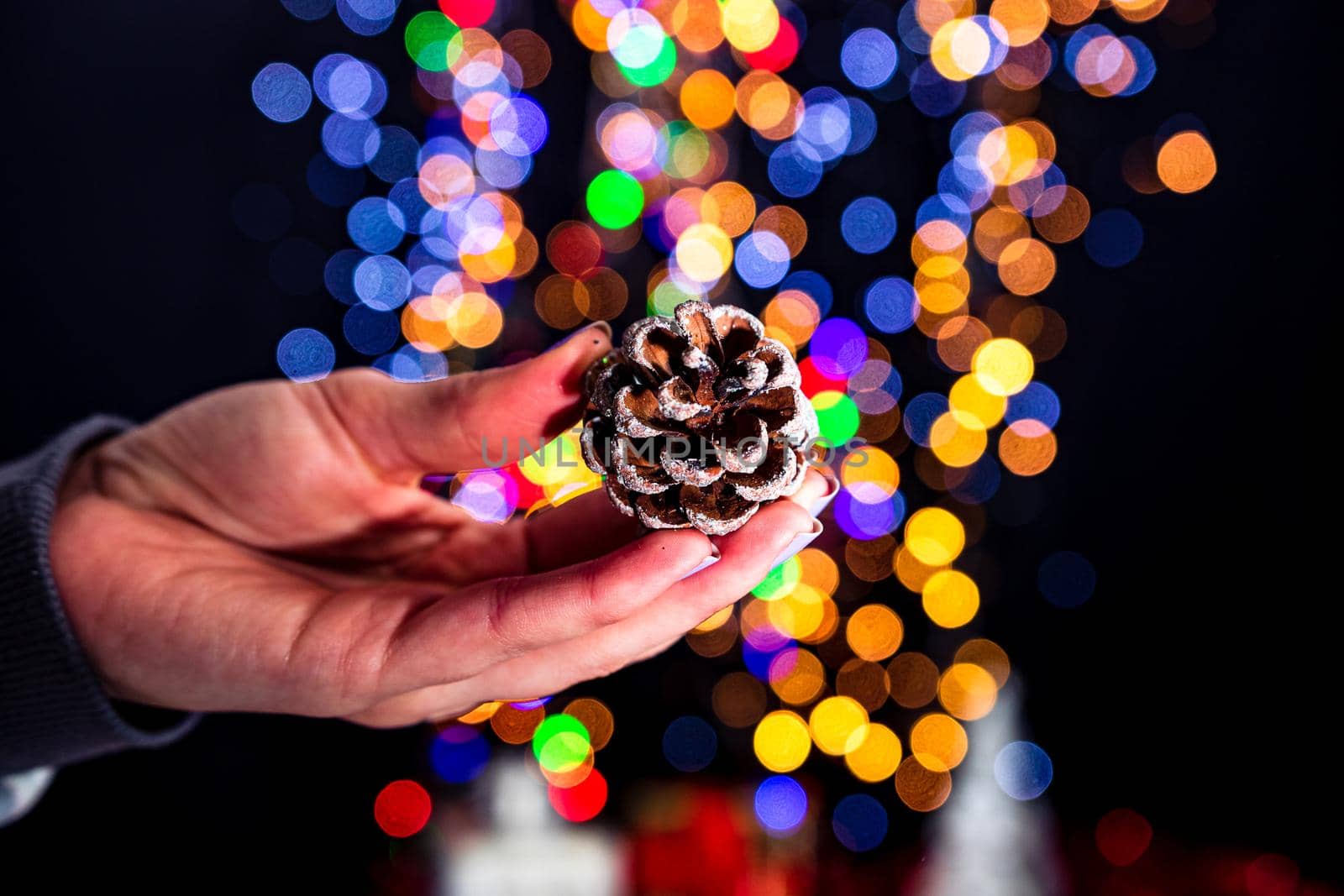 Holding Christmas pine cone decoration isolated on background with blurred lights. December season, Christmas composition.