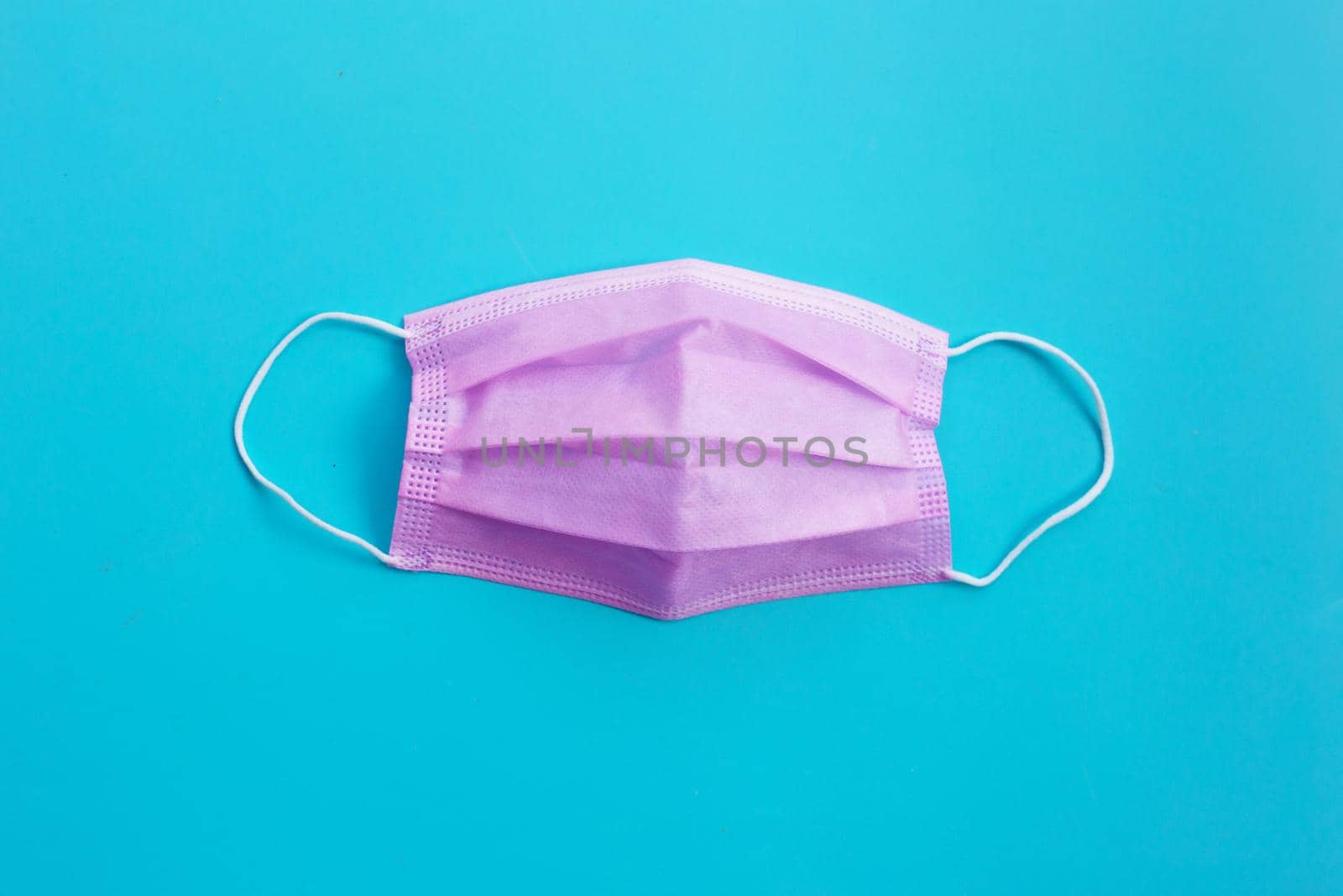 Pink protective medical mask on blue background. Top view