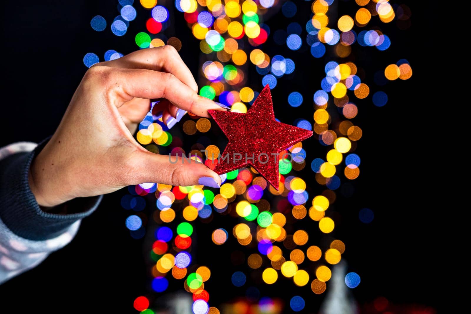 Holding Christmas glittery star decoration isolated on background with blurred lights. December season, Christmas composition.