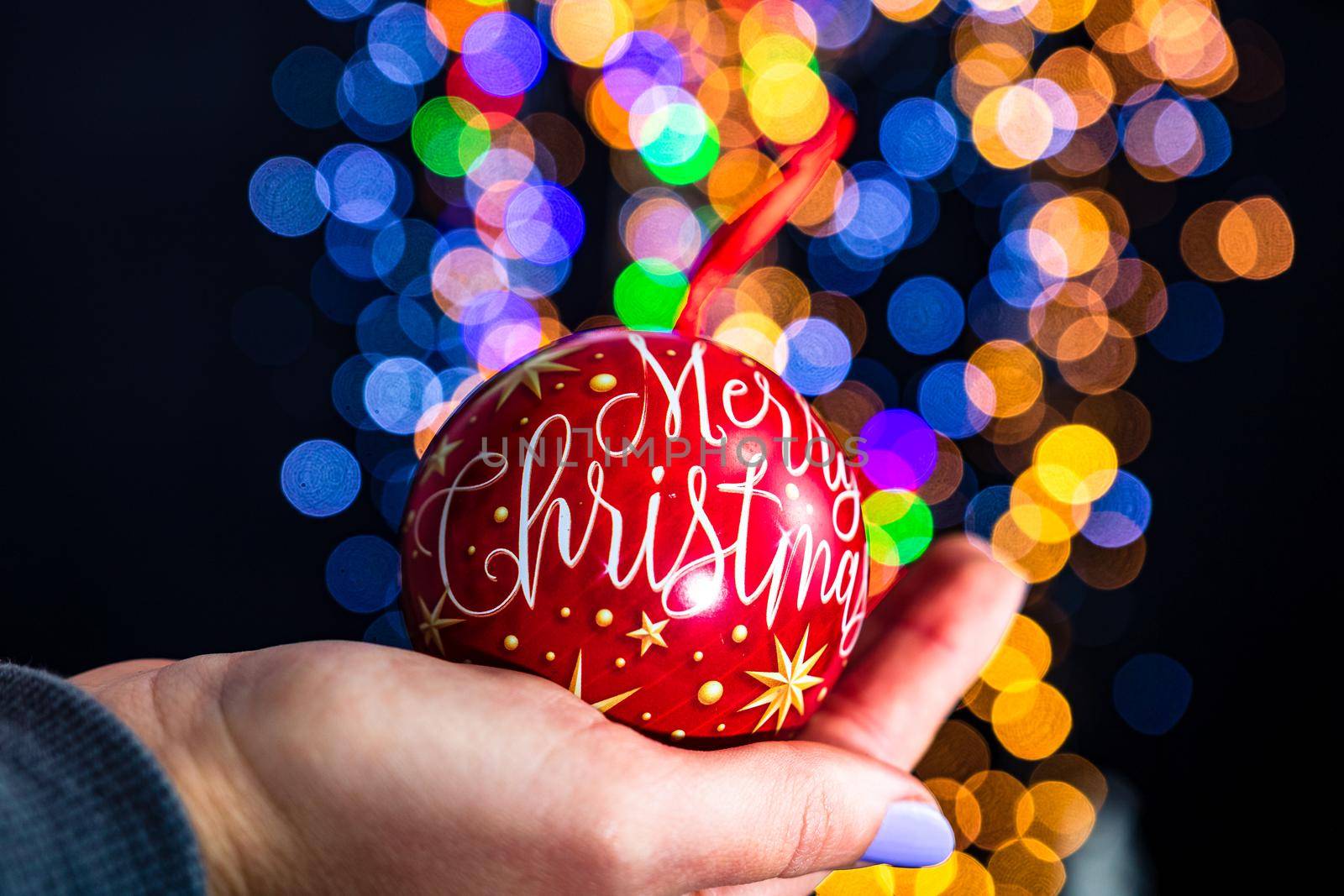 Holding Merry Christmas bauble decoration isolated on background with blurred lights. December season, Christmas composition.