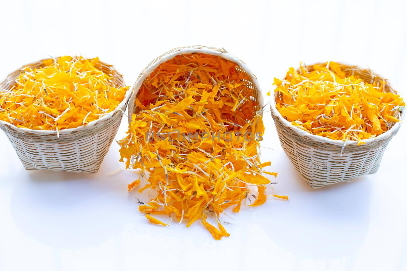 Marigold flower petals in bamboo basket on white background.