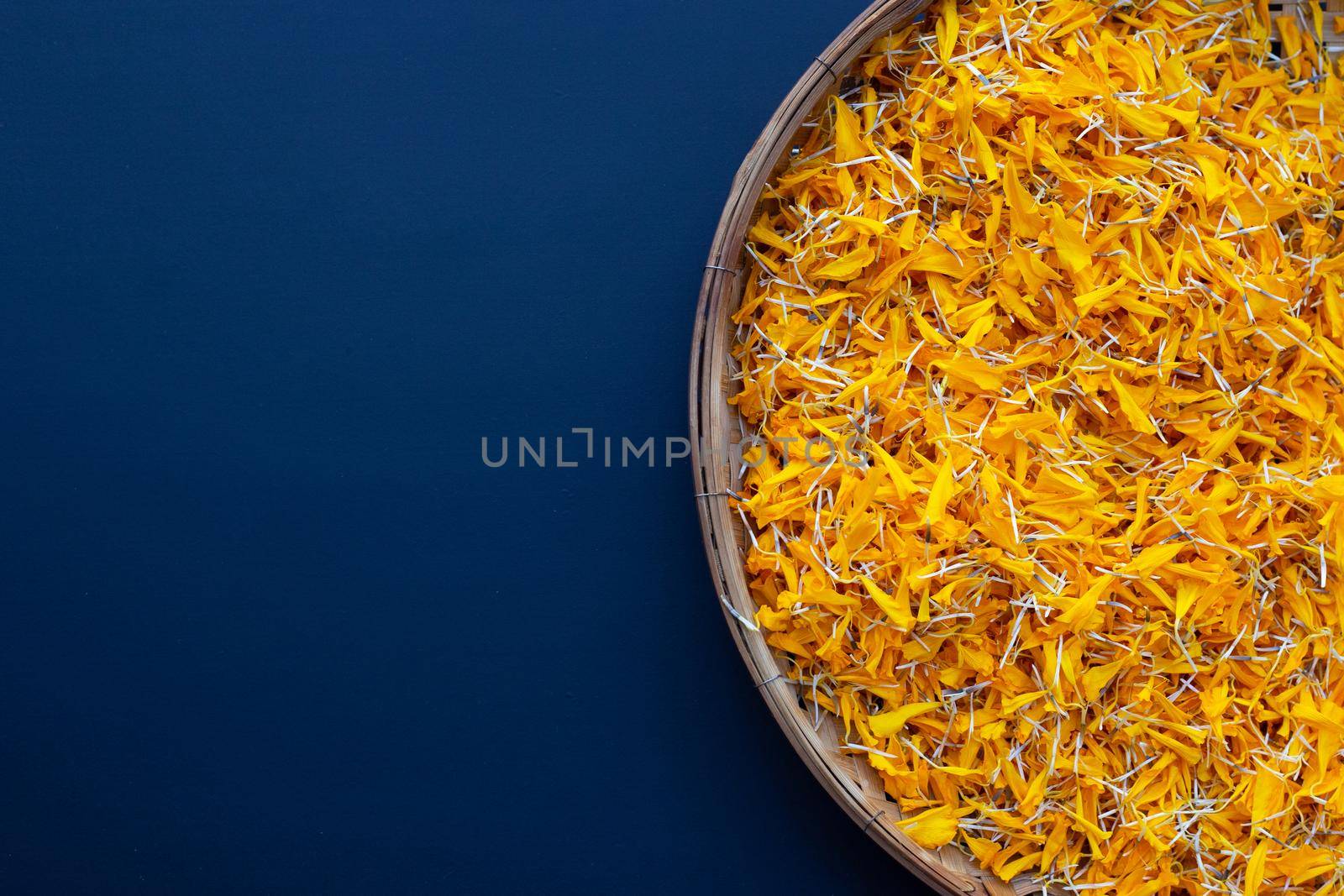 Marigold flower petals in wooden bamboo threshing basket on dark background.