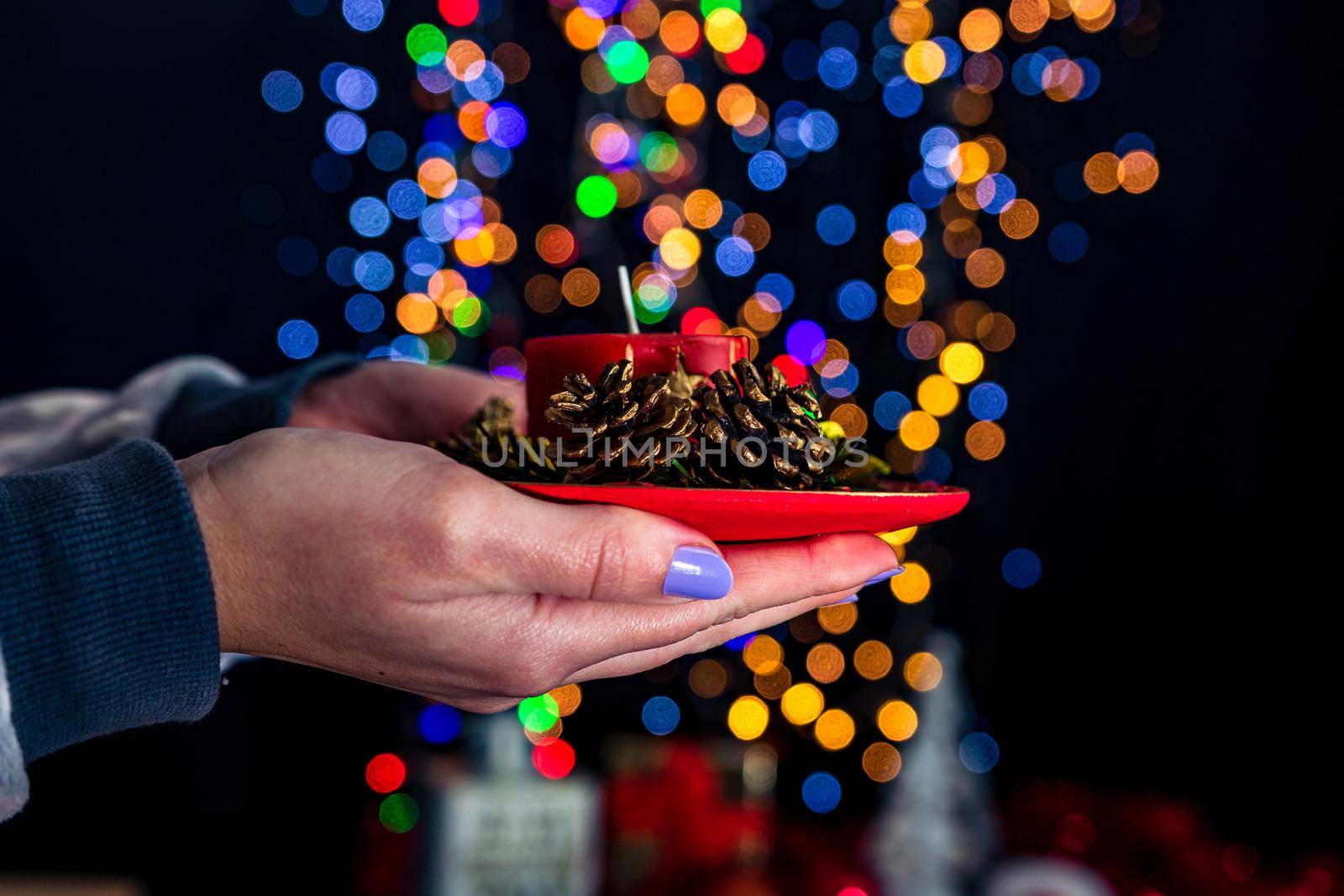 Holding Christmas decorated candle isolated on background with blurred lights. December season, Christmas composition.
