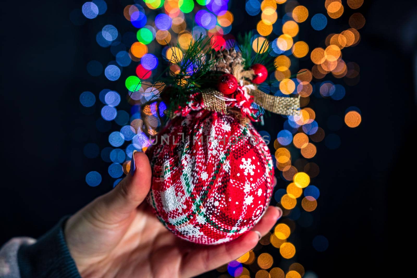 Holding Christmas bauble decoration isolated on background with blurred lights. December season, Christmas composition.