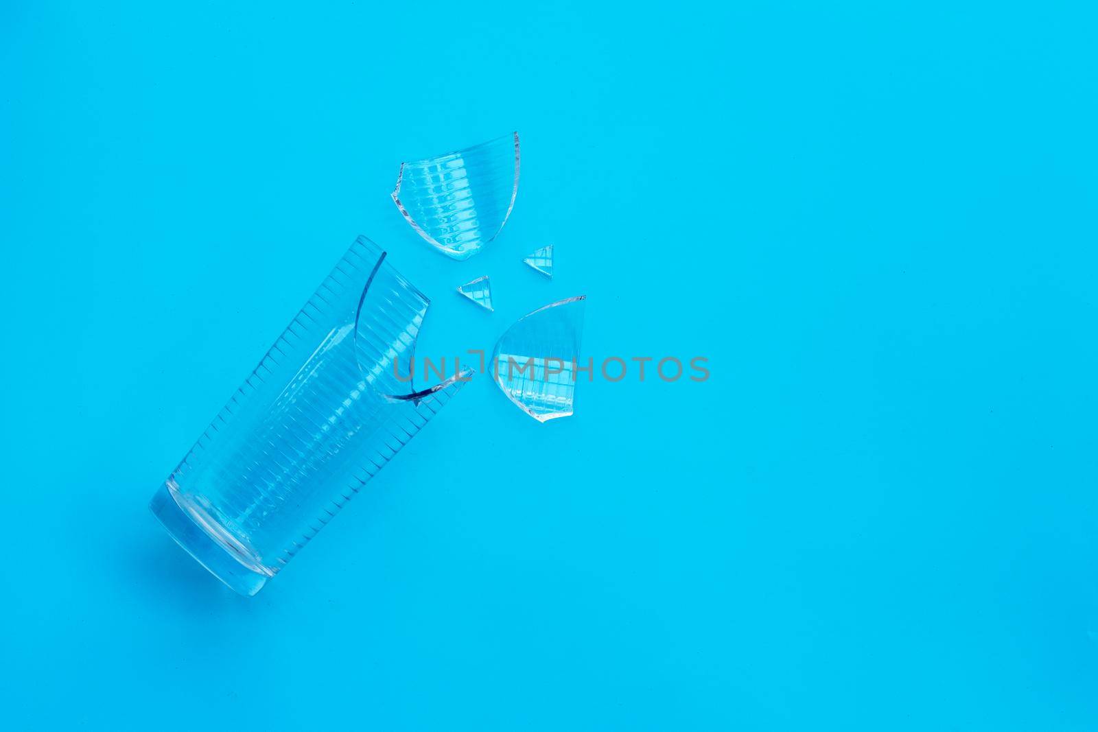 Empty broken drinking glass on blue background. Copy space